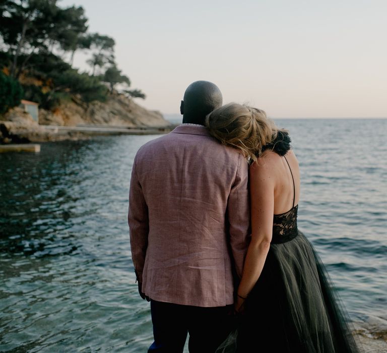 Bride in Vera Wang black wedding dress cosies up to groom whilst overlooking the ocean