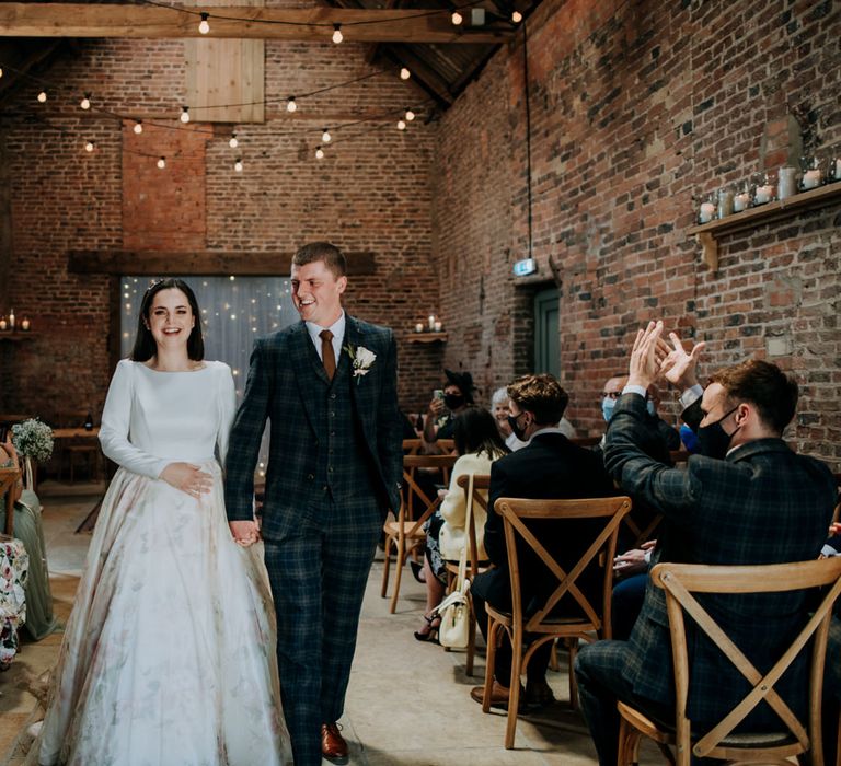 Groom in navy check suit holding hands with his bride in a couture wedding dress with pink floral patterned skirt 