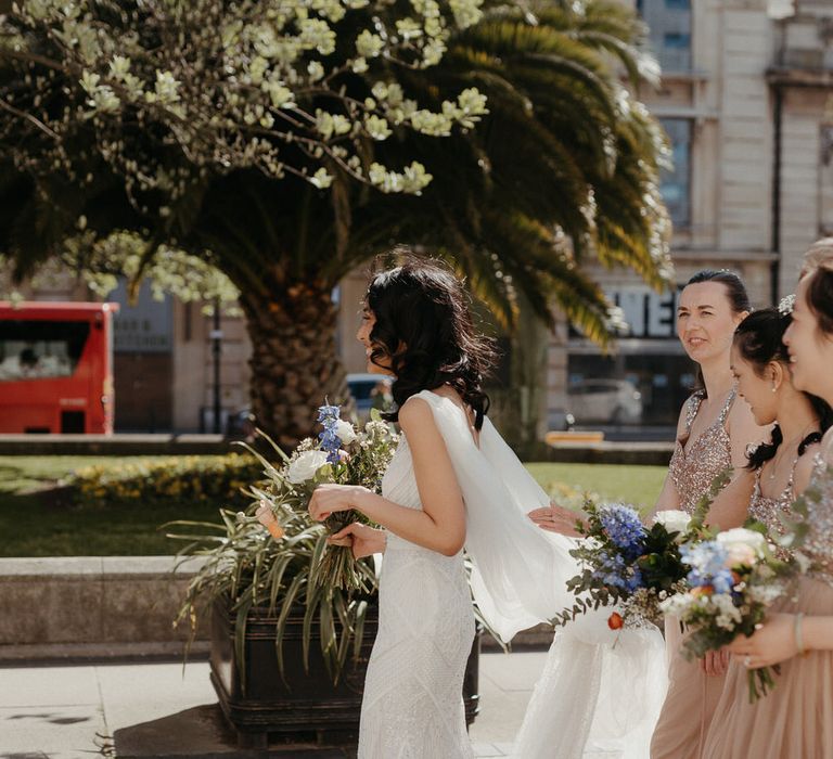 Bridesmaids walking behind the bride holding her veil outside Hackney Town Hall