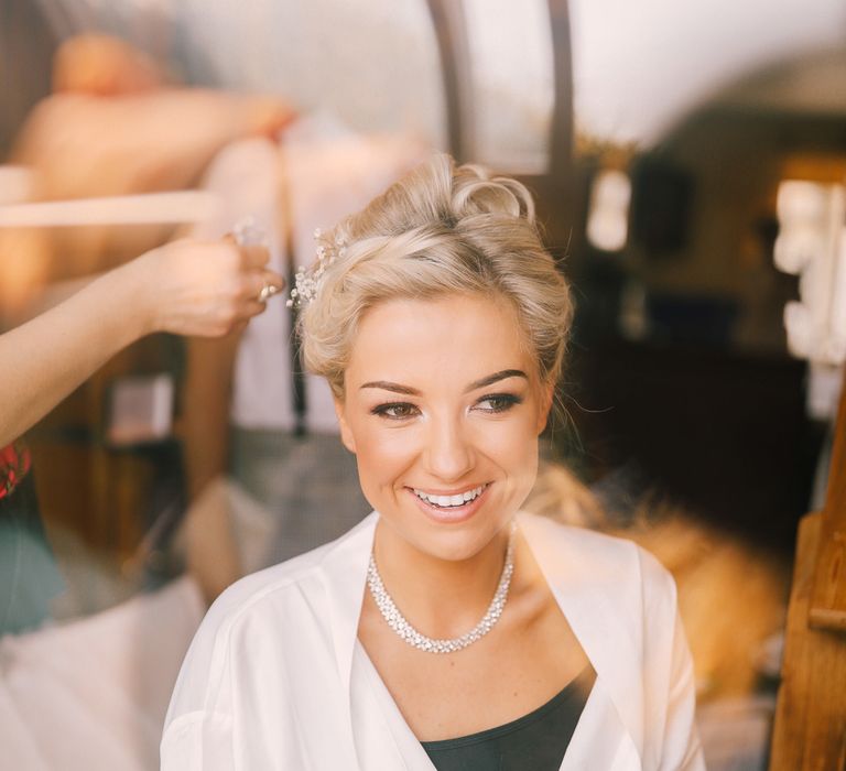 A blonde bride wearing a white robe gets gypsophelia put into her hair as she gets ready for her wedding. 