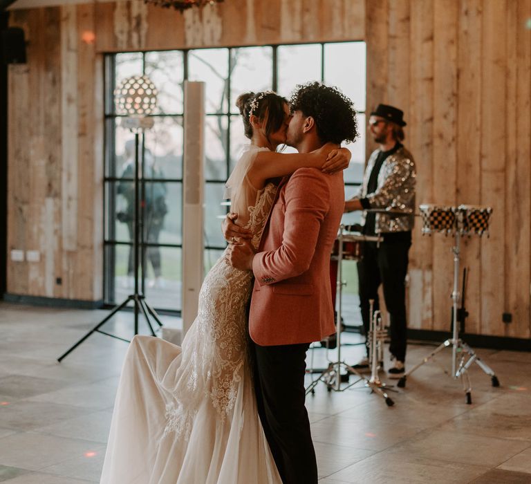 First dance with groom in a red blazer kissing his bride in a tulle and lace wedding dress with bow shoulder detail on the dance floor 