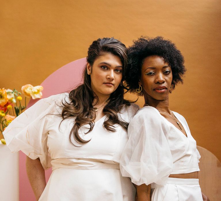 Two brides leaning on each other wearing matching Paper To Lace wedding separates with puff sleeves and long maxi skirt