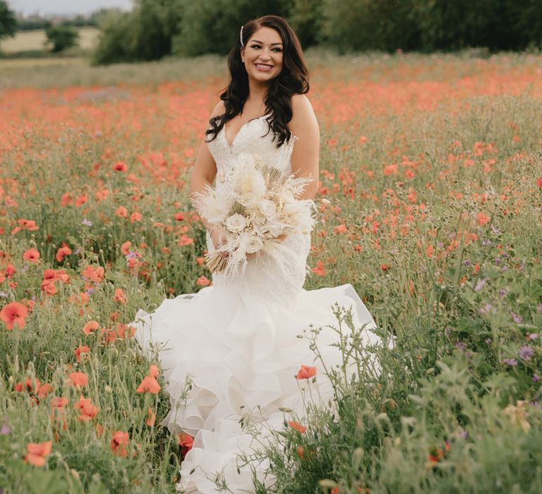 Beautiful bride standing in a poppy field in a Mori Lee fishtail wedding dress holding a neural dried flower wedding bouquet 