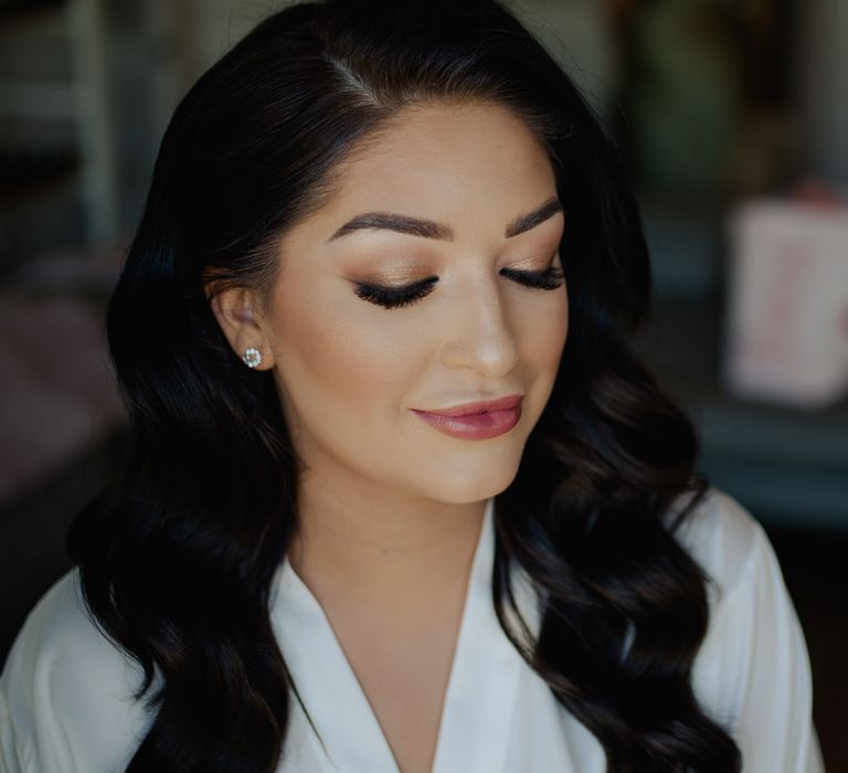 Bride with long wavy side swept hair and flawless bridal makeup with shimmering eyeshadow and deep pink lipstick. 