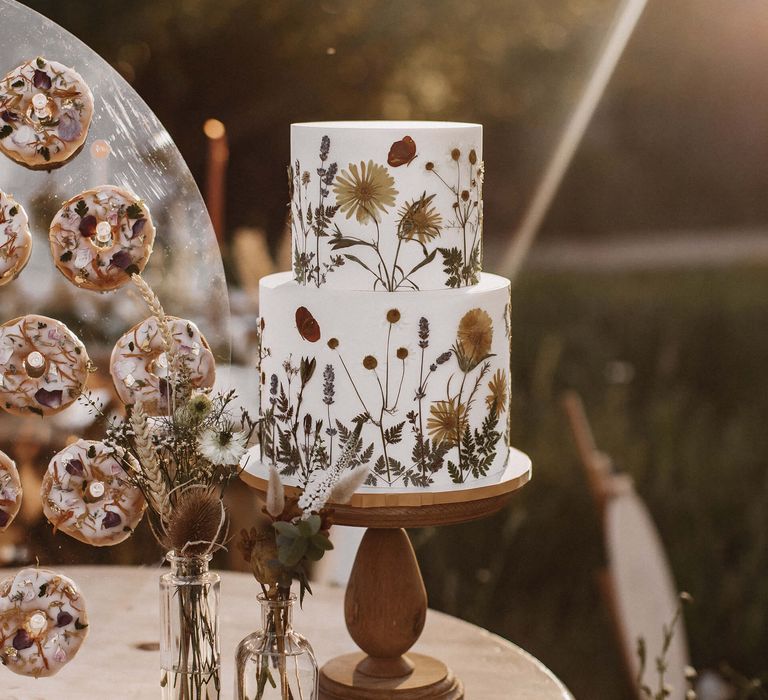 Two tier buttercream wedding cake with edible flower pressed design on a wooden cake stand 