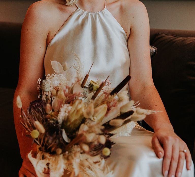 Beautiful bride with shoulder length wavy hair in a halter neck champagne colour wedding dress holding a dried flower wedding bouquet 