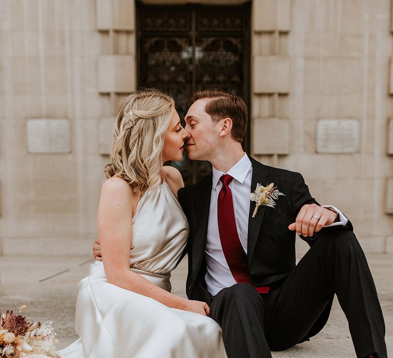 Bride in a Kate Beaumont champagne colour wedding dress kissing her groom in a black suit and burgundy tie on the steps at Leeds Civic Hall 