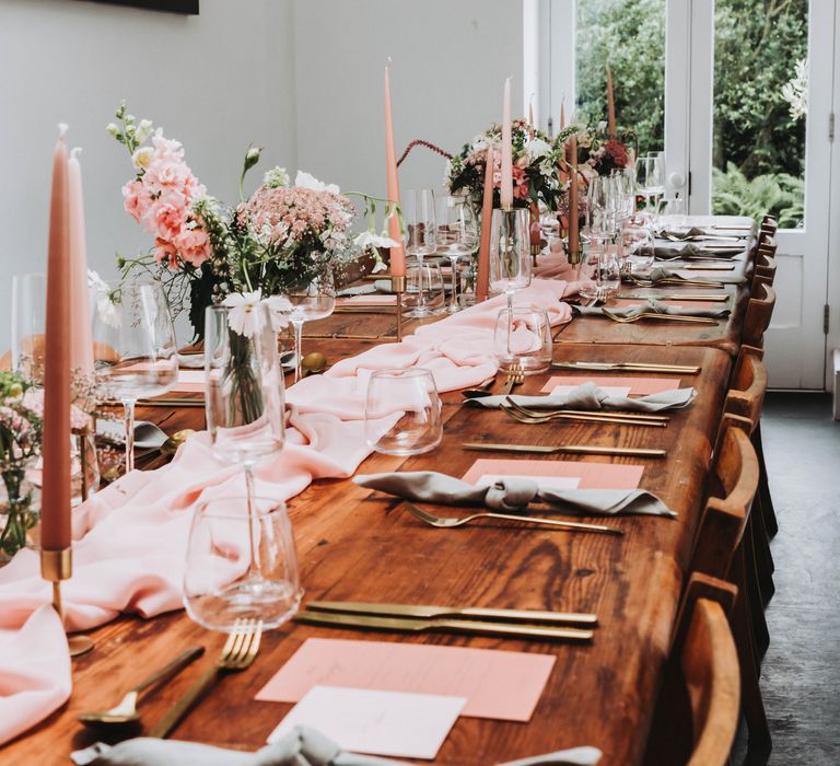 Pastel pink and peach colour scheme for tablescape complete with pink cloth table runner, pink candles and gold cutlery