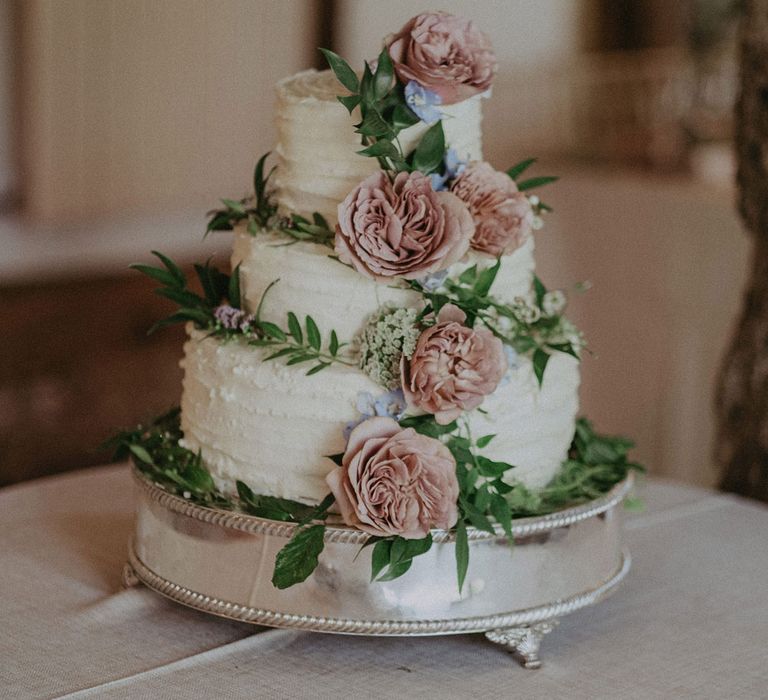 Three tier buttercream wedding cakes with green foliage and pink floral details on silver cake stand for Loseley Park wedding in Surrey