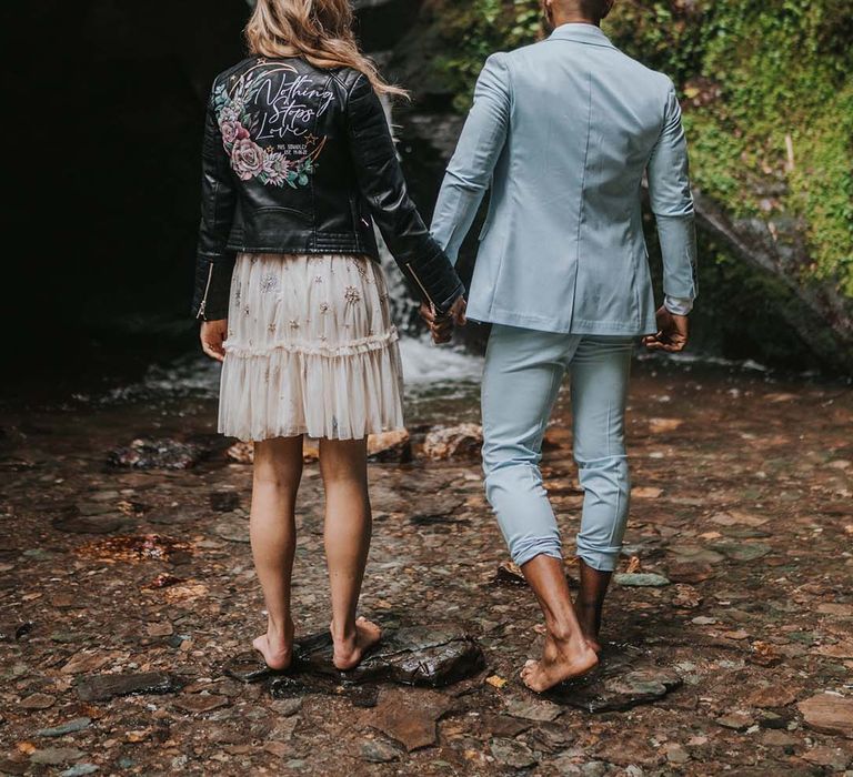 Bride & groom walk hand in hand after wedding ceremony through waterfall in Cornwall