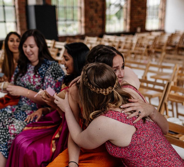 Wedding guests in brightly coloured wedding dresses sit in the front row on wooden folding chairs in the wedding ceremony room at Loft Studios London