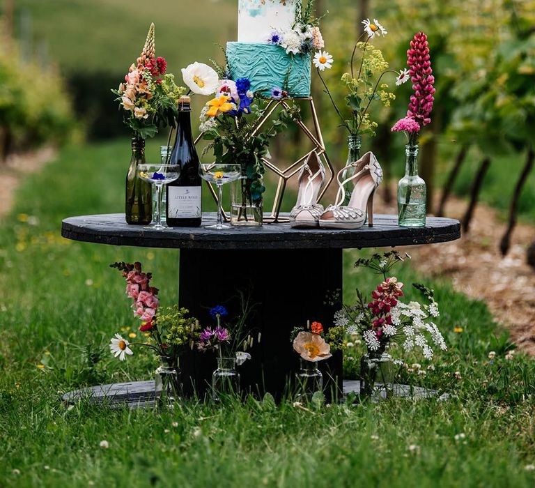 turquoise and white buttercream wedding cake wresting on a cotton wheel surrounded by colourful wildflowers at Little Wold Vineyard