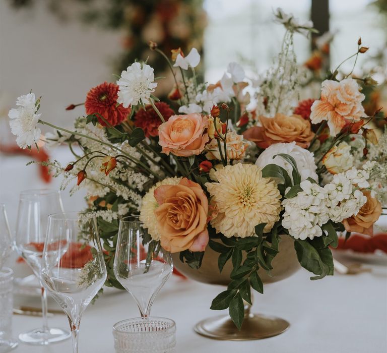 Wedding flower centrepiece with orange, peach, yellow and white flowers in a gold vessel 