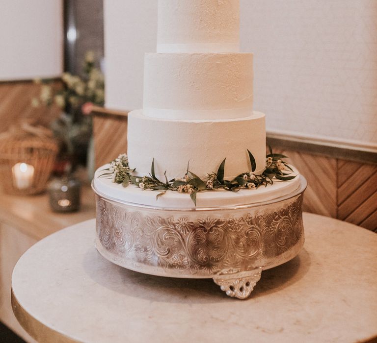 Three-tier white wedding cake with a foliage hoop wedding cake topper 