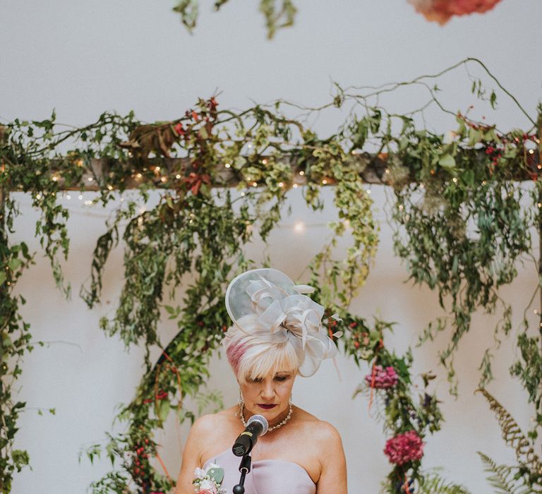 Wedding guest reads during ceremony whilst wearing pale pink dress