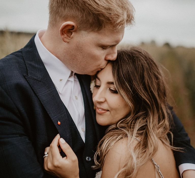 Bride leans into her groom as he kisses her forehead on wedding day