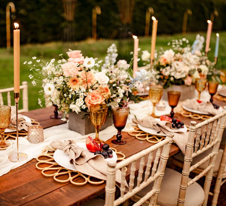 Rustic wooden wedding table with pastel florals, amber glassware and pastel dinner candles for outdoor wedding breakfast