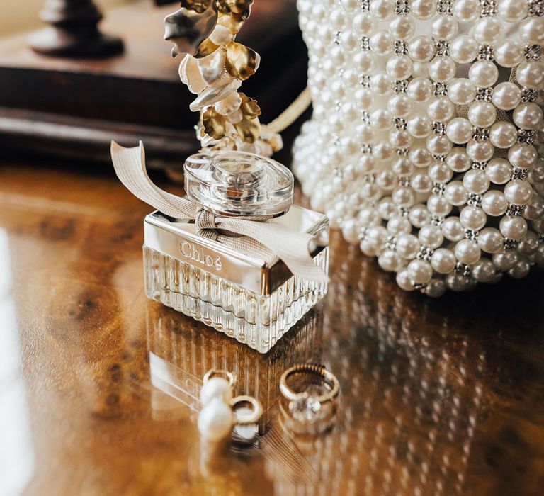 Bespoke floral headband, Chloé perfume, pearl earrings and diamond wedding ring on wooden table