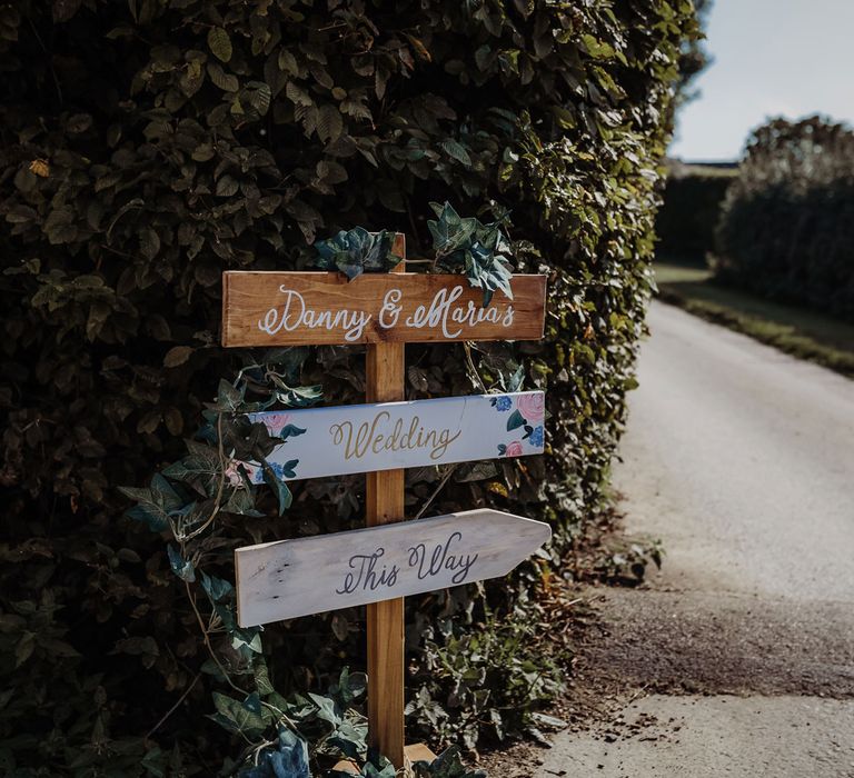 Rustic wooden wedding signs on pole reading 'Danny & Maria's wedding this way' on side of road for Cotswolds wedding