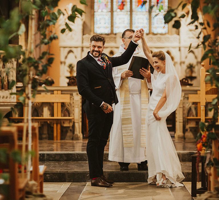 Bride and groom holding hands at the altar of their church wedding ceremony decorated with trees 