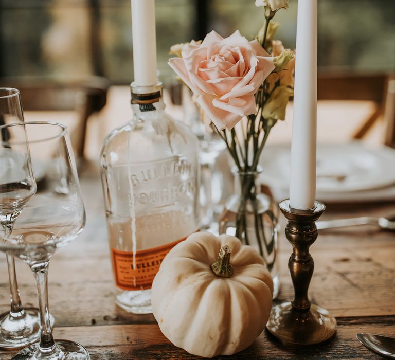 Pink rose in glass bud vase with candles and small white pumpkin for rustic wedding table decor