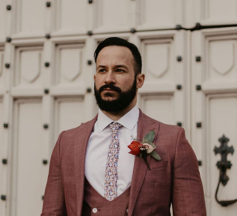 Bearded groom in a deep pink three-piece suit with horseshoe waistcoat and floral tie 