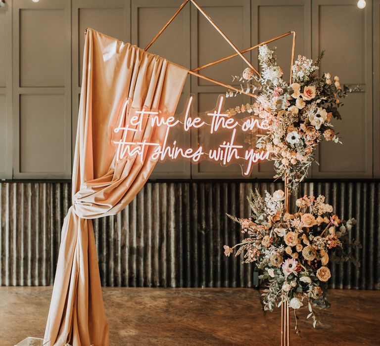 Gold Fram wedding arch with pink draping, mixed flower clouds and pink neon wedding sign