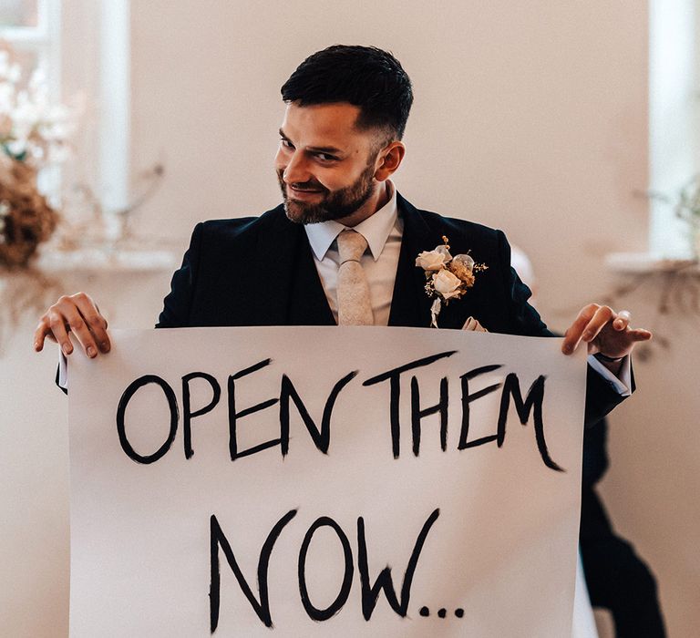 Groomsman in a navy suit holding up a banner during the wedding ceremony for a surprise moment 