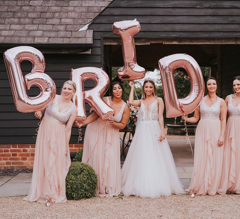 Bride and bridesmaids in stunning pink dresses in front of 'bride' balloons