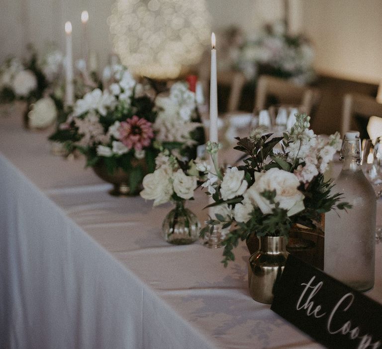 Top table wedding tablescape with pink and white flowers in assorted vases and tall white tapered candles 