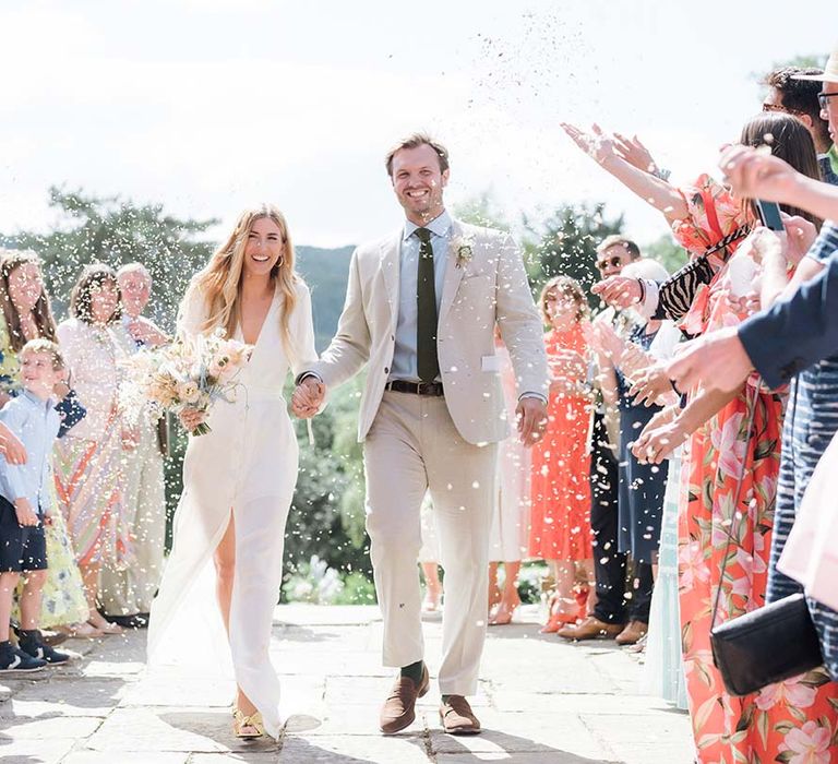 Bride in bespoke Bon Bride dress and groom have their confetti exit at their garden wedding in summer in Bath