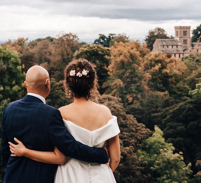 Bride and groom in blue checkered suit look out at the view of wedding venue