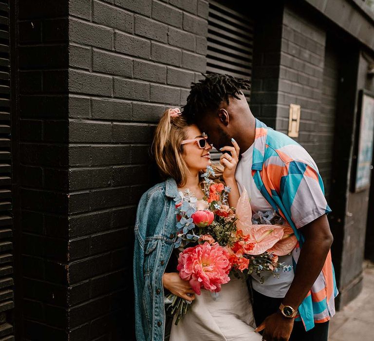 Groom in a patterned shirt embracing his bride in a short wedding dress and denim jacket at their stylish urban elopement 