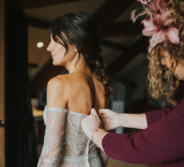 Bride gets help getting into her off the shoulder Zavana couture wedding dress with sparkles