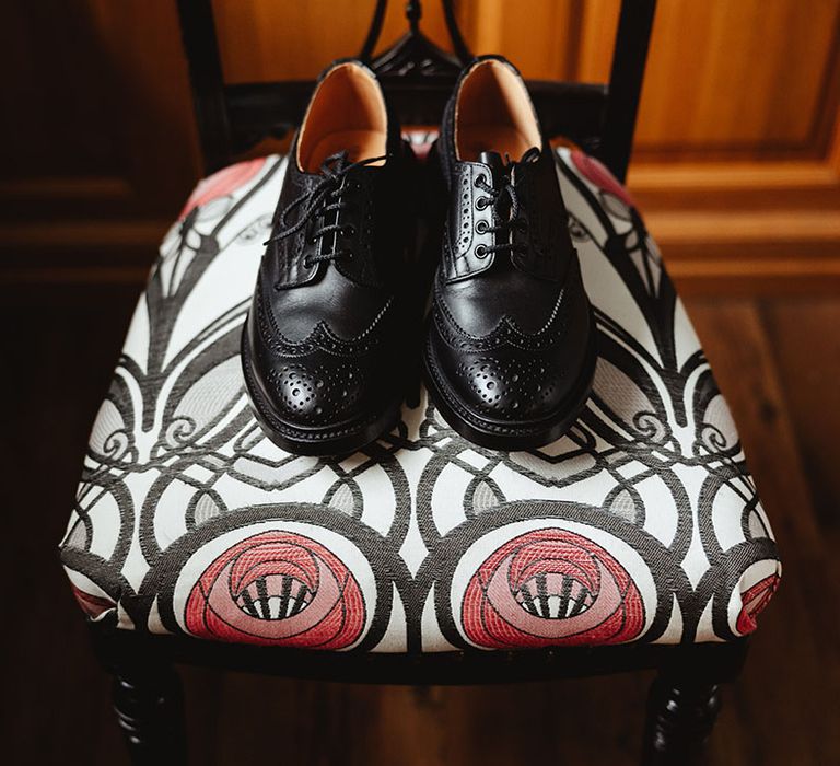 Black shined brogue wedding shoes for groom on patterned chair 