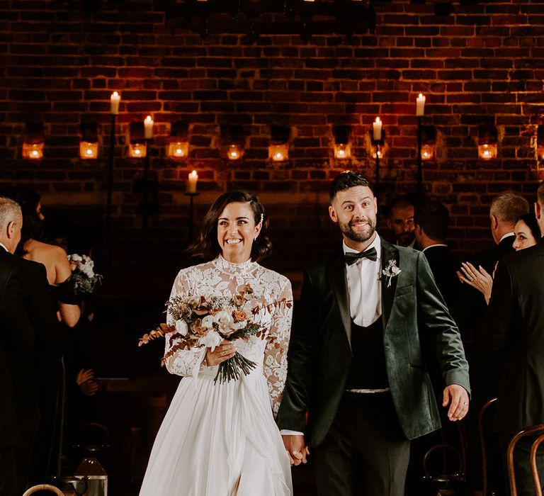 Groom looks stunned in black tie outfit as he leaves ceremony with bride in sweetheart illusion lace wedding dress