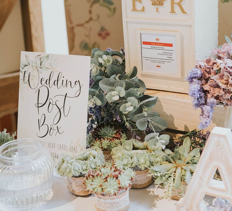 White painted postbox with personalised details next to sign with leaf detail requesting cards of congratulations on a table surrounded by plants