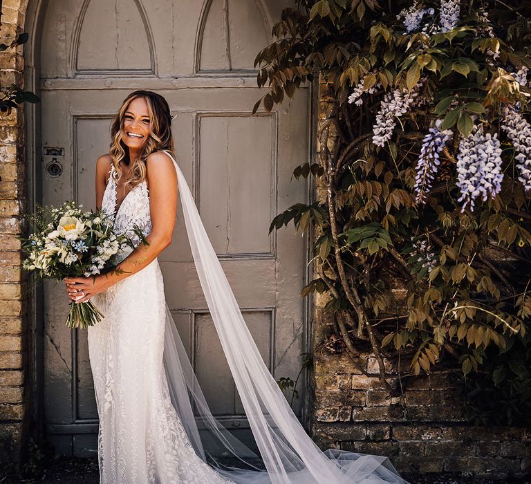 Bride holding yellow and blue bouquet with bride in lace wedding dress with train and detachable tulle wings 