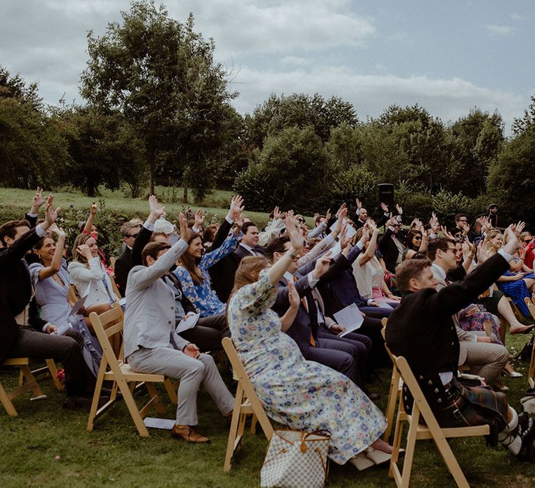 Wedding guests raise their hands as part of the outdoor wedding ceremony at Owlpen Manor 