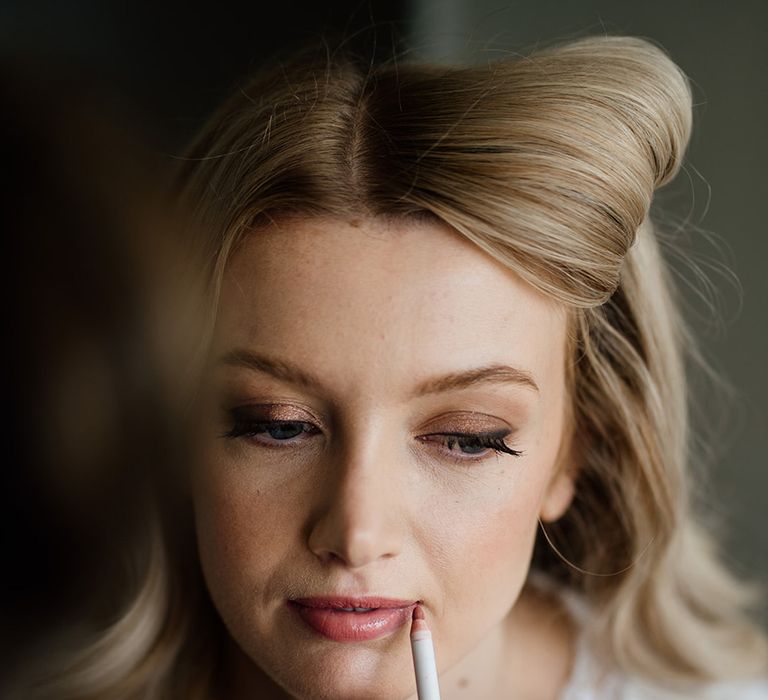 Bride gets her makeup done with a pink lip and gold eyeshadow with a soft wing 