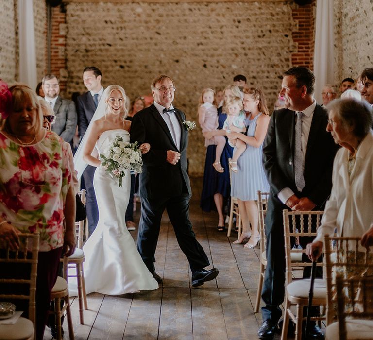 Father of the bride in black tie walks the bride down the aisle to the groom 