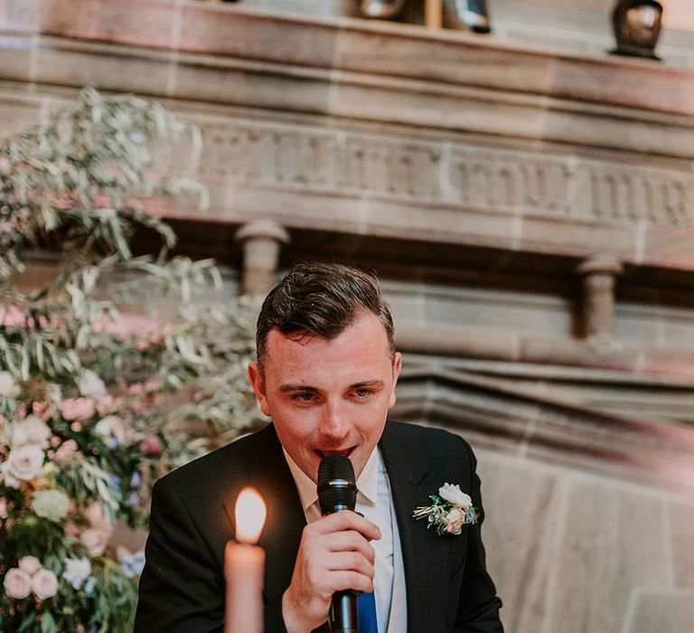 Groom wears pastel coloured floral buttonhole and morning suit whilst giving speech during wedding reception