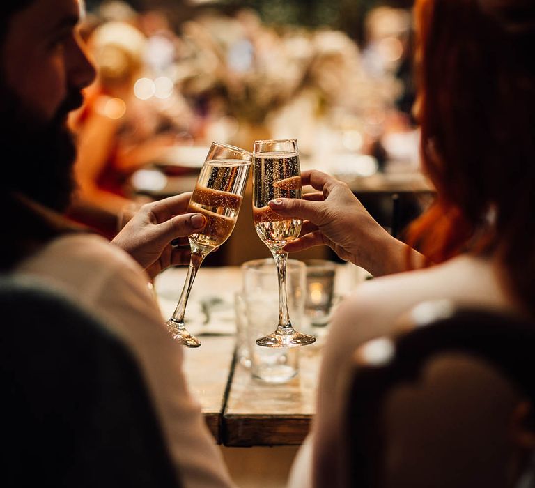 Bride and groom clink their glasses together in a cheers 