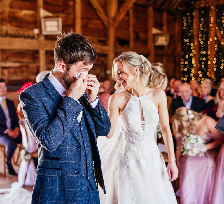 Groom in blue checkered suit wipes tears with a tissue as he sees the bride for the first time 