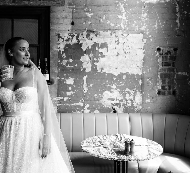 Bride wears fitted sparkly wedding dress and holds margarita on the morning of her wedding day in Brixton 