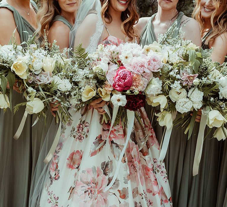 Bride and bridesmaids hold out their wedding bouquets with white and pink flowers and foliage 