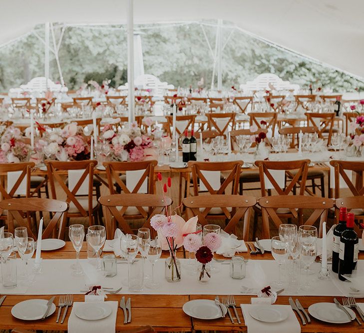 Wooden banquet tables in marquee with white and pink wedding flowers 