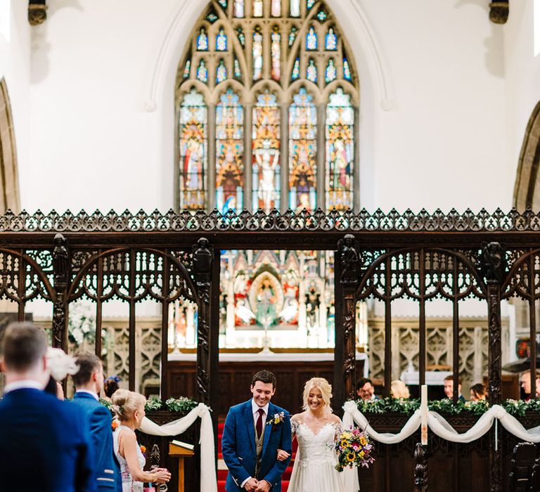 Bride holds bright floral bouquet as she walks down the aisle with her groom after church wedding ceremony 