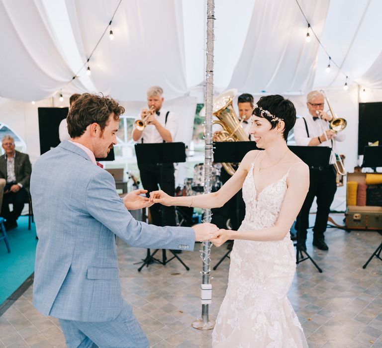 Bride wearing Enzoani lace wedding dress & groom in dusty blue suit dance in secondhand marquee on their wedding day