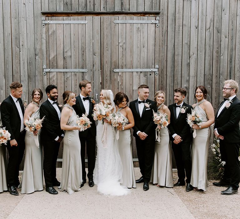 Wedding party shot with the men in black tie, bridesmaids in sage green halter neck dresss and the bride and groom 